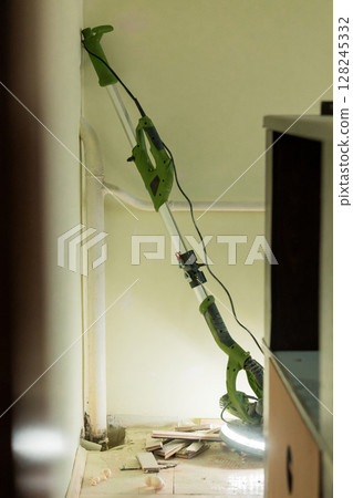 Indoor Home Renovation with Green Electric Pole Saw. Dust, Debris, and Exposed Wall in a Partially Demolished Room, Remodeling Process 128245332