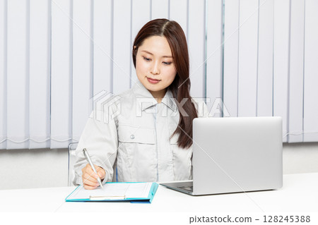 Woman in work clothes operating a PC and taking notes 02 Woman in work clothes operating a PC and taking notes 02 128245388