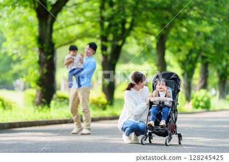 Parents and children walking in a stroller through a park with fresh greenery Parents and children walking in a stroller through a park with fresh greenery 128245425