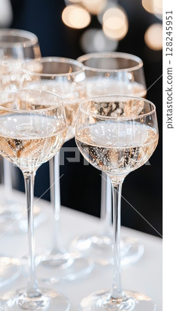 Elegant champagne glasses brimming with sparkling champagne positioned on table, soft warm lighting blurring background, evoking celebration and festivity Elegant champagne glasses brimming with sparkling champagne positioned on table, soft warm lighting blurring background, evoking celebration and festivity 128245951