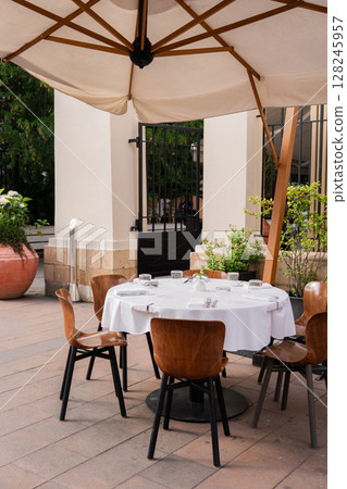 An Elegant Outdoor Dining Setup Featuring Stylish Umbrella and Comfortable Chairs 128245957