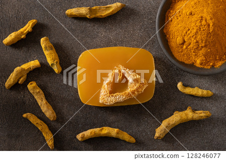 Turmeric soap bar and powder turmeric root on dark brown background. Organic skincare product perfect for wellness, beauty, and organic body care concepts. View from above. 128246077