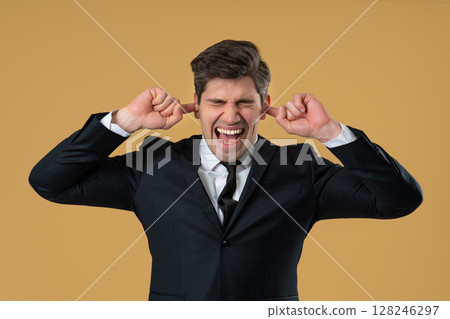Businessman covering ears, showing irritation in beige studio. Stress, overload 128246297