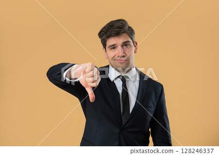Businessman in suit giving thumbs down dislike with disapproving look on beige Businessman in suit giving thumbs down dislike with disapproving look on beige 128246337