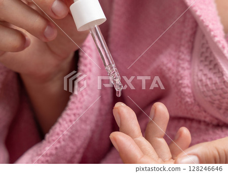 Young woman in pink bathrobe dropping essential oil on a finger and holding a pipette closeup Young woman in pink bathrobe dropping essential oil on a finger and holding a pipette closeup 128246646