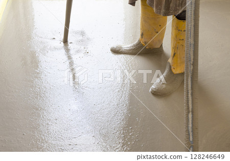 Worker wearing yellow rubber boots pouring concrete over floor in a new house construction site. Worker wearing yellow rubber boots pouring concrete over floor in a new house construction site. 128246649