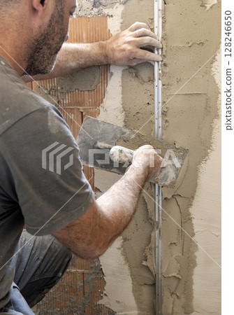 Craftsman uses a float trowel and cement to plaster a house wall. Construction process 128246650