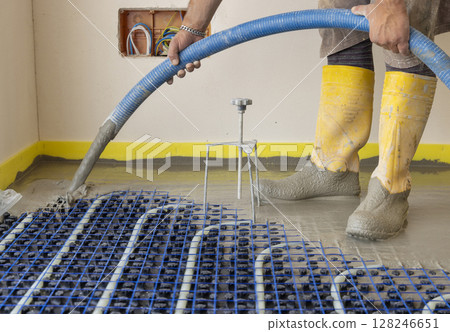 Man pouring concrete over floor heating installation in a new building. Modern construction system Man pouring concrete over floor heating installation in a new building. Modern construction system 128246651