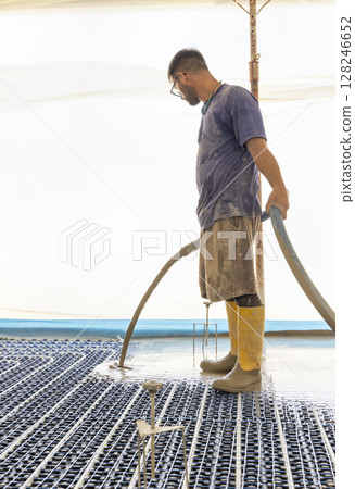 Man pouring concrete over floor heating installation in a new building. Modern construction system Man pouring concrete over floor heating installation in a new building. Modern construction system 128246652
