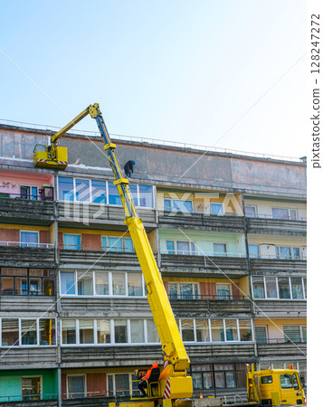 Workers on Boom Lift Repair Facade of Residential Apartment Building Under Clear Blue Sky Workers on Boom Lift Repair Facade of Residential Apartment Building Under Clear Blue Sky 128247272