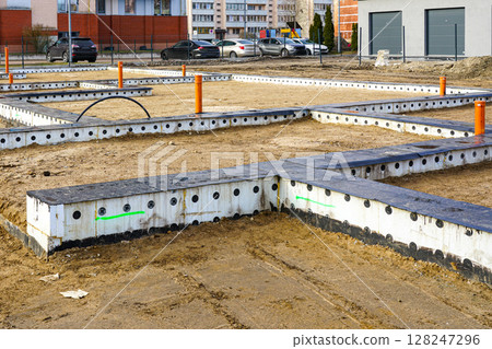 Modern building foundation under construction with insulated forms, utility pipes, structural layout Modern building foundation under construction with insulated forms, utility pipes, structural layout 128247296
