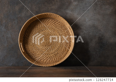 Round woven wicker basket, tray or plate stand on brown background. Asian Style Bamboo basket. Round woven wicker basket, tray or plate stand on brown background. Asian Style Bamboo basket. 128247714
