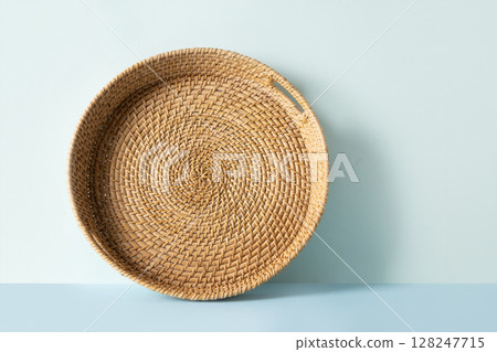 Round woven wicker basket, tray or plate stand on blue background. Handmade by local craftsmen in sri lanka traditional tableware. Round woven wicker basket, tray or plate stand on blue background. Handmade by local craftsmen in sri lanka traditional tableware. 128247715