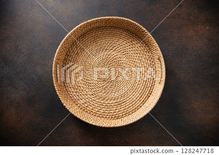 Round Woven wicker basket, tray or plate on dark rustic surface. Handmade by local craftsmen in sri lanka traditional tableware. View from above 128247718