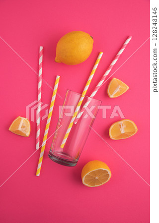 Preparing lemonade. Lemons, straws, and a glass on a vibrant pink background. 128248146