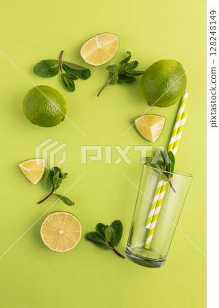 Preparing lemonade. Border from limes, mint leaves, straws, and a glass on a vibrant green background. Preparing lemonade. Border from limes, mint leaves, straws, and a glass on a vibrant green background. 128248149