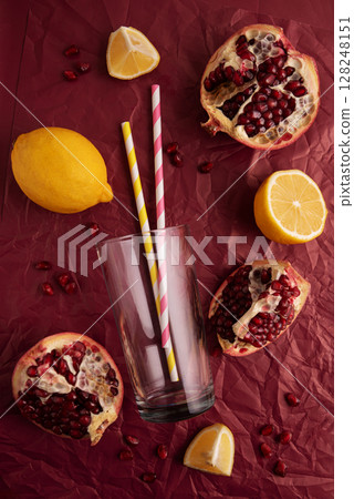 Preparing lemonade. Pomegranates, lemons, straws, and a glass on a red background. Preparing lemonade. Pomegranates, lemons, straws, and a glass on a red background. 128248151