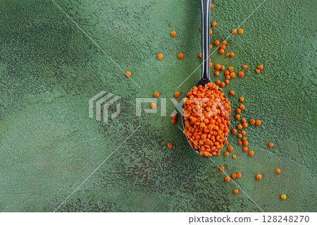 Vibrant orange lentils on a silver spoon against a green textured background showcase culinary potential and natural ingredients Vibrant orange lentils on a silver spoon against a green textured background showcase culinary potential and natural ingredients 128248270