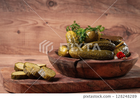 Pickled cucumbers in a wooden bowl with herbs and spices, close-up, rustic style, 128248289