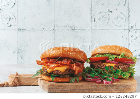 two burgers with beef patty, fried bacon, cheddar cheese, tomatoes, on a light table, two burgers with beef patty, fried bacon, cheddar cheese, tomatoes, on a light table, 128248297