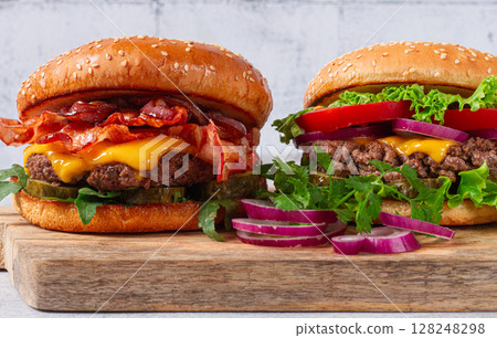 two burgers with beef patty, fried bacon, cheddar cheese, tomatoes, on a light table, 128248298