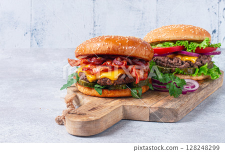 two burgers with beef patty, fried bacon, cheddar cheese, tomatoes, on a light table, two burgers with beef patty, fried bacon, cheddar cheese, tomatoes, on a light table, 128248299