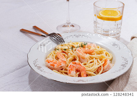 Pasta with shrimp and thyme, served on a white plate, with a glass of white wine, the table is set, there are no people, Pasta with shrimp and thyme, served on a white plate, with a glass of white wine, the table is set, there are no people, 128248341