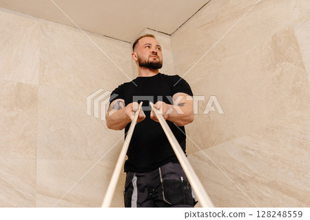 Construction worker installing ceramic tiles on bathroom wall using level tool 128248559
