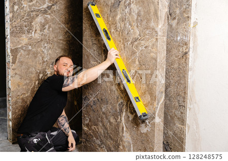 Construction worker using spirit level installing marble tile on wall 128248575