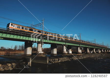一列中央線快速列車(E233系列)在清晨的陽光下穿過一座鐵路橋 一列中央線快速列車(E233系列)在清晨的陽光下穿過一座鐵路橋 128248587