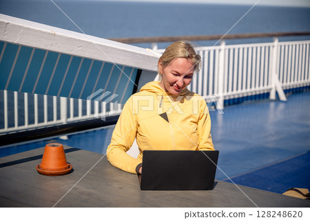Woman working on laptop outdoors on ferry deck on sunny windy day 128248620