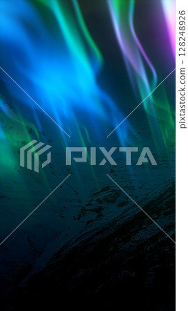 Stylized aurora lights in vibrant green and purple tones above a dark landscape 128248926