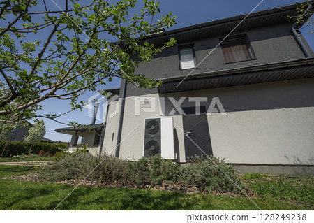 Energy-efficient heat pump system mounted on a modern house wall in a green residential area 128249238
