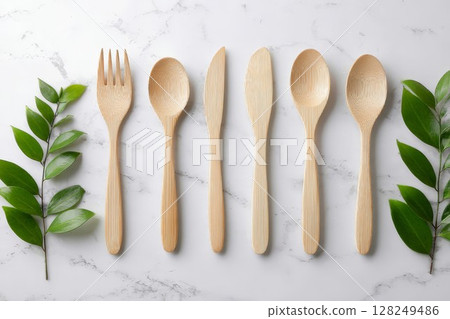 Wooden cutlery set with green leaves on marble background. Eco friendly utensils include fork, spoon, knife, perfect for sustainable kitchen use. 128249486