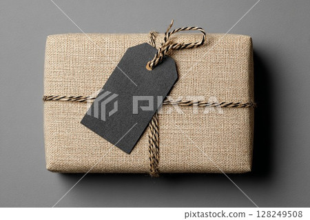 Gift box wrapped in burlap with black tag and twine. Rustic package on gray background perfect for branding. Ideal for holiday or special occasion design. Gift box wrapped in burlap with black tag and twine. Rustic package on gray background perfect for branding. Ideal for holiday or special occasion design. 128249508