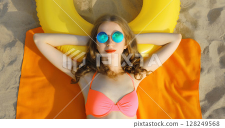 Summer vacation, happy relaxing young woman lying on sand on sea beach with swimming inflatable ring Summer vacation, happy relaxing young woman lying on sand on sea beach with swimming inflatable ring 128249568