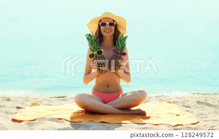 Summer vacation, happy smiling young woman with pineapple in hat with sunglasses lying on sea beach 128249572