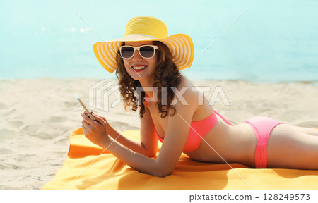 Summer vacation, happy young woman with phone, beautiful girl holding smartphone lying on sea beach 128249573