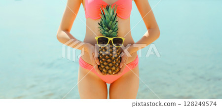Summer vacation, close up beautiful young woman with pineapple in bikini swimsuit on sea beach Summer vacation, close up beautiful young woman with pineapple in bikini swimsuit on sea beach 128249574