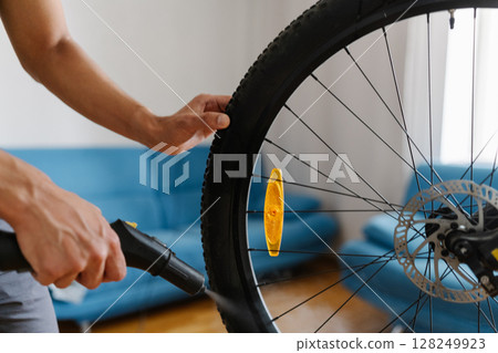 Man owner bike cleaning dirty dusty tire of bicycle wheel using steam cleaner, ensuring thorough cleaning in apartment environment, close-up. Concept of bike maintenance and service. 128249923