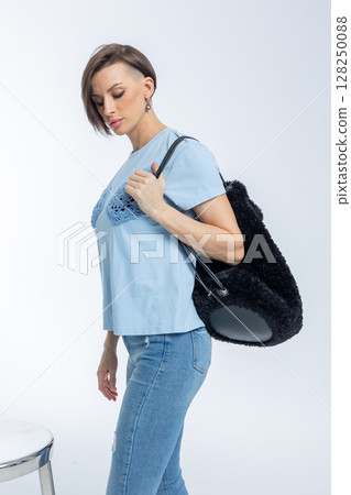 Beautiful woman of model appearance. Girl in blue clothes with black bag on grey background. Pretty female with trendy makeup posing in studio. Vertical photo. High quality photo Beautiful woman of model appearance. Girl in blue clothes with black bag on grey background. Pretty female with trendy makeup posing in studio. Vertical photo. High quality photo 128250088
