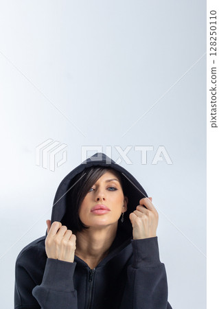 Portrait beautiful woman of model appearance. Girl in black sweatshirt on grey background. Pretty female with trendy makeup posing in studio. Vertical photo. High quality photo 128250110