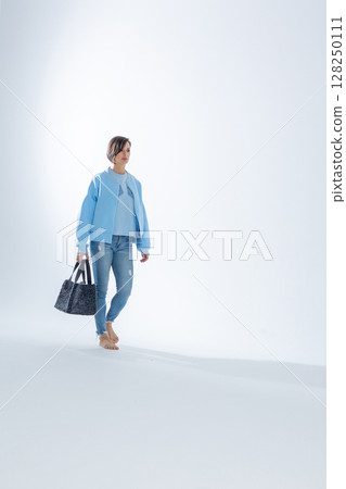 Beautiful woman of model appearance. Girl in blue clothes with black bag on grey background. Pretty female with trendy makeup posing in studio. Vertical photo. High quality photo 128250111
