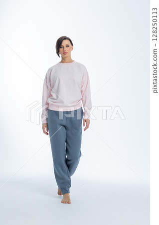 Beautiful woman of model appearance. Girl in light pink jumper and gray trousers on light background. Pretty female with trendy makeup posing in studio. Vertical photo. High quality photo 128250113