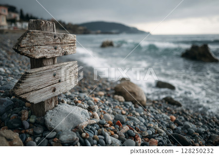 Rustic wooden signpost stands on rocky beach near sea waves 128250232