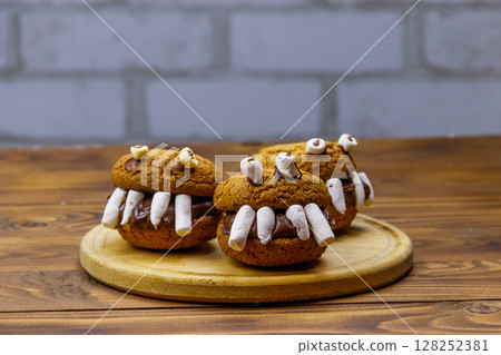 Halloween dessert: Toothed monsters made of oatmeal cookies, chocolate spread and marshmallows on a wooden table Halloween dessert: Toothed monsters made of oatmeal cookies, chocolate spread and marshmallows on a wooden table 128252381