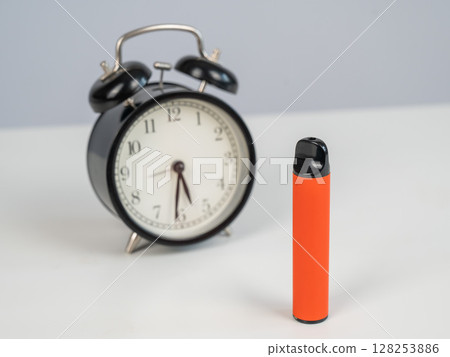 Disposable vape and alarm clock on white background. Disposable vape and alarm clock on white background. 128253886