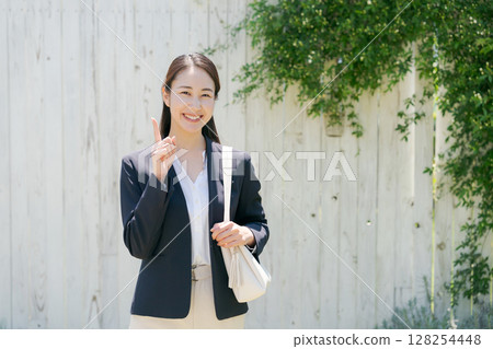 一位身穿西裝的女士站在白牆前 128254448