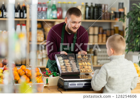 Friendly seller offers cookies to little customer in grocery store Friendly seller offers cookies to little customer in grocery store 128254606