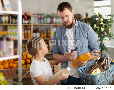 European man with son customer at shop scans QR code on drink bottle using phone camera 128254627